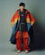 Person wearing a colorful coat and red pants against a plain background
