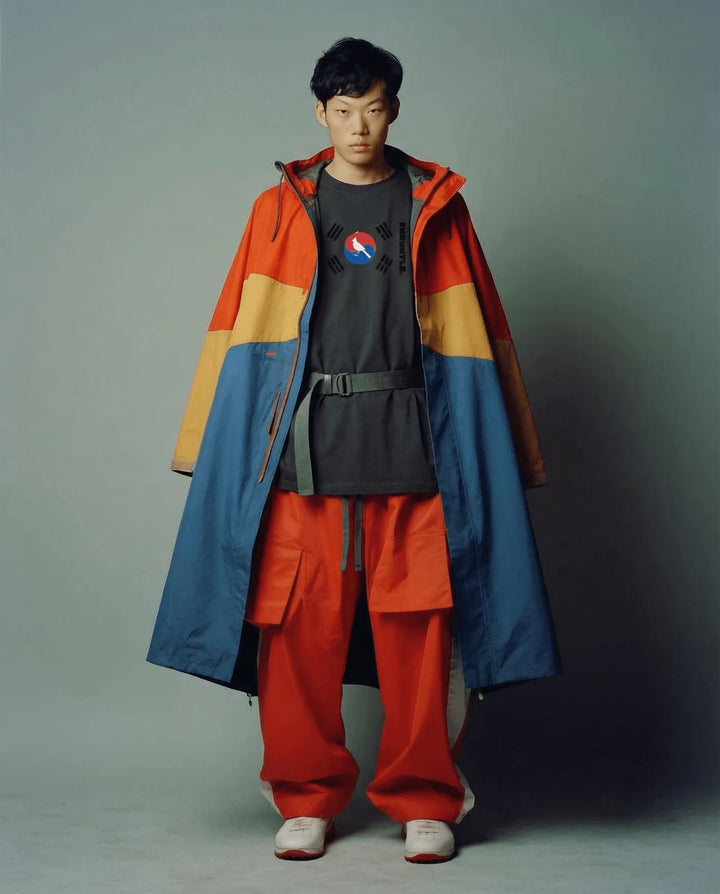 Person wearing a colorful jacket and red pants against a plain background