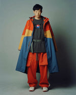 Person wearing a colorful jacket and red pants against a plain background