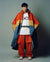 Person wearing a colorful jacket and red pants with a white shirt featuring a logo.