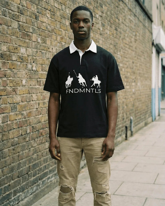 Man wearing a black polo shirt with white collar and graphic design, standing against a brick wall.