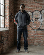 Cotton oversized hoodie in snow washed black with loose fit, worn by male model in urban setting. Features red sleeve print and kangaroo pocket.