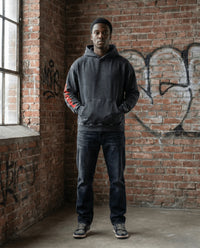 Cotton oversized hoodie in snow washed black with loose fit, worn by male model in urban setting. Features red sleeve print and kangaroo pocket.
