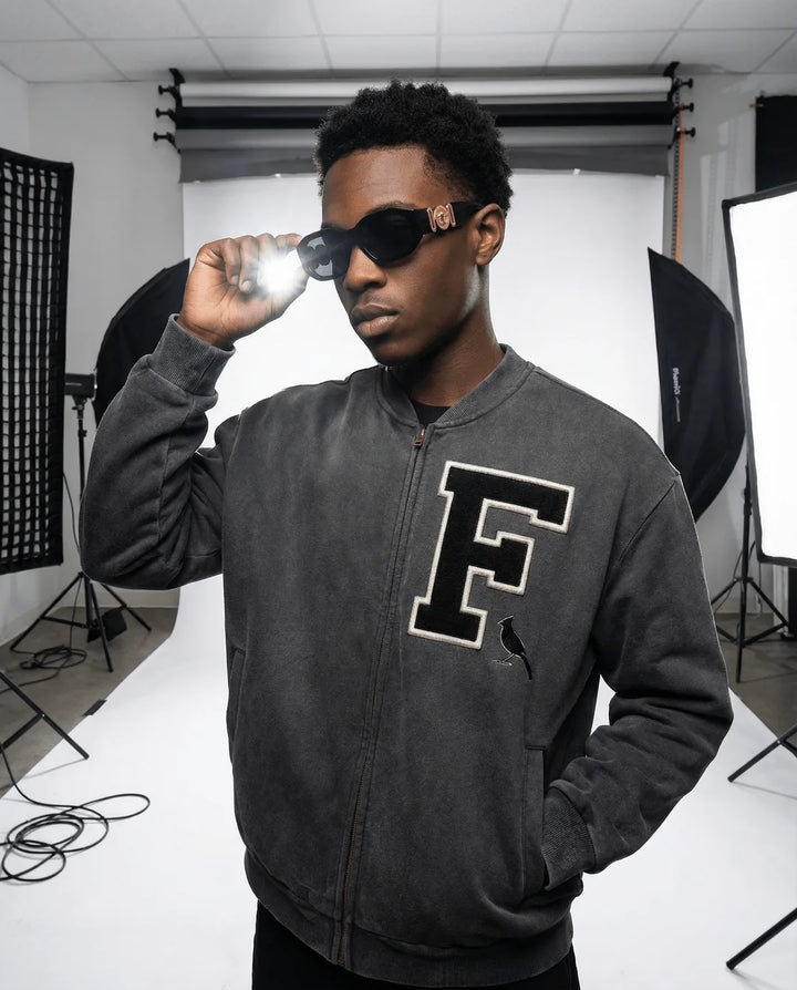 Unisex Vintage Washed Fleece Baseball Jacket in charcoal gray with oversized fit and varsity 'F' patch, modeled in a studio setting.