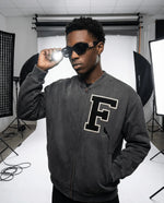 Unisex Vintage Washed Fleece Baseball Jacket in charcoal gray with oversized fit and varsity 'F' patch, modeled in a studio setting.