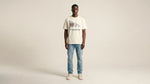 Man wearing a white t-shirt with text and blue jeans on a beige background