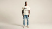 Man wearing a white t-shirt with text and blue jeans on a beige background