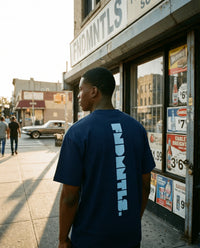 Man wearing a navy blue t-shirt with 'FNDMNTLS' branding standing on a city street.