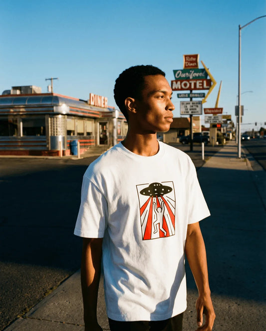 Person wearing a white t-shirt with a graphic design in front of a diner and motel sign.