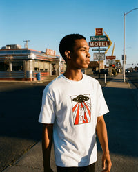 Person wearing a white t-shirt with a graphic design in front of a diner and motel sign.
