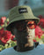 Person wearing a beige bucket hat with a brand logo and sunglasses, standing in front of red flowers.