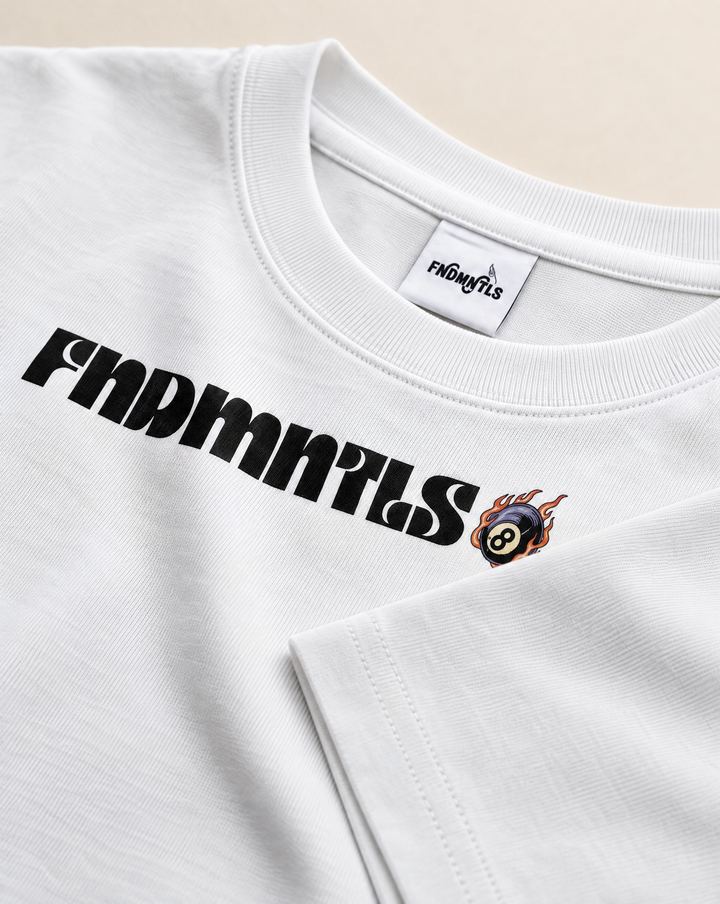 Close-up of a white crewneck t-shirt featuring a black 'FINDMNTS' logo across the chest and a small flaming billiards 8-ball graphic next to it. The inner neck label also displays the 'FINDMNTS' brand name.