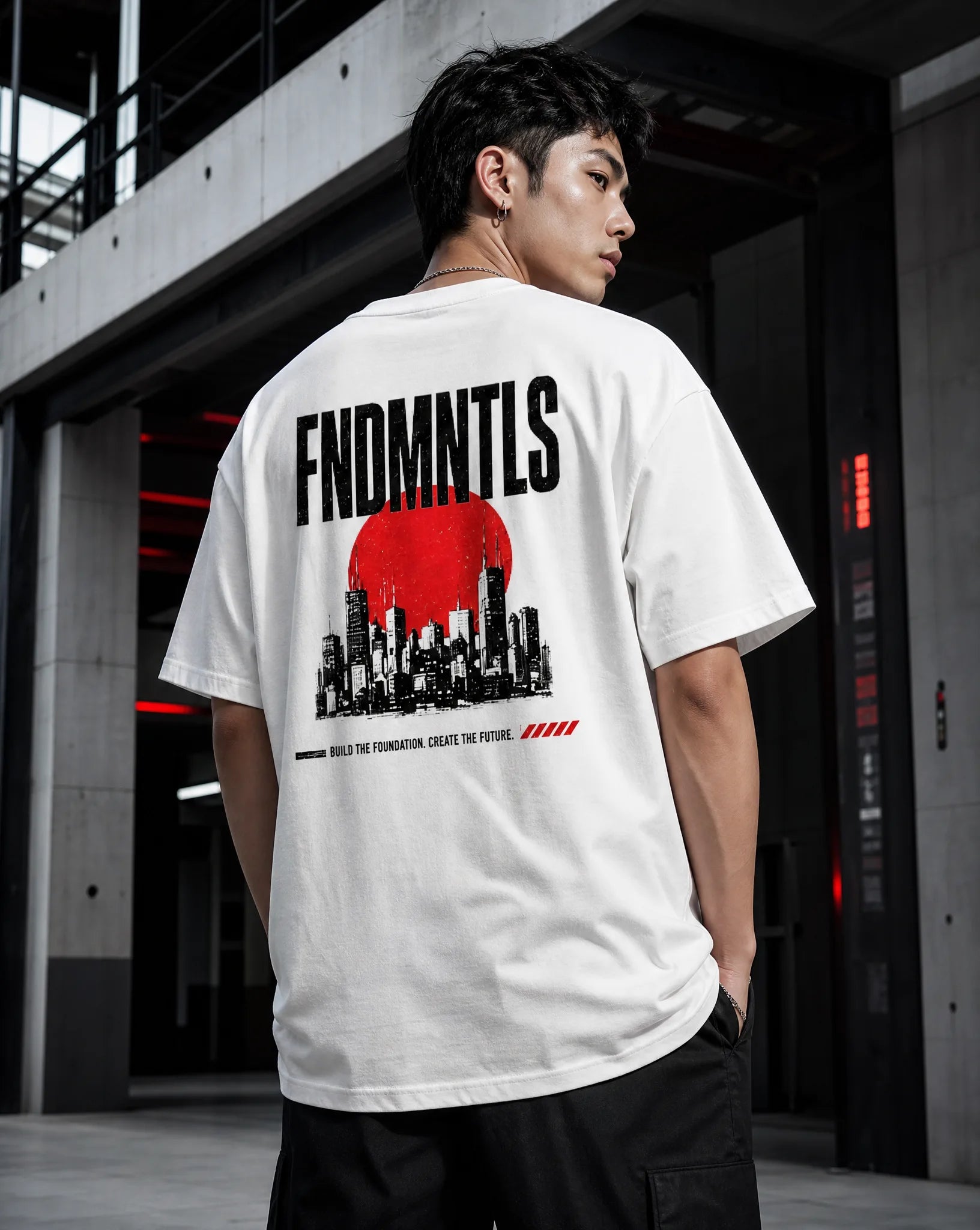 A man wearing a white t-shirt with a large black and red graphic print on the back, standing in a modern concrete industrial setting.