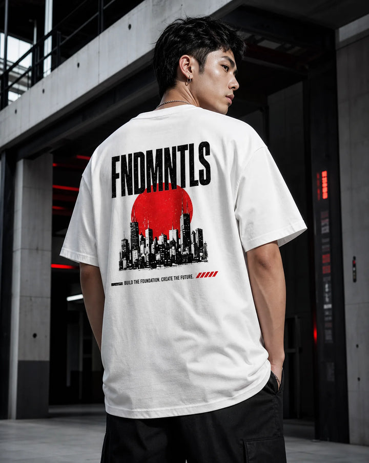 A man wearing a white t-shirt with a large black and red graphic print on the back, standing in a modern concrete industrial setting.