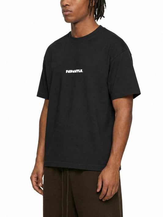 A man wearing a black crewneck t-shirt with the brand name 'FUGAWANT.' printed in white on the chest, paired with brown pants, against a plain white background.