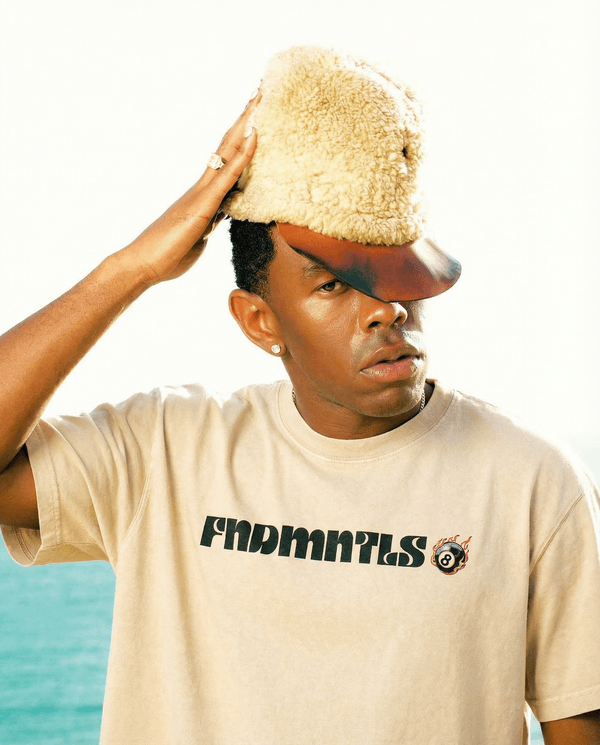 Model wearing Mineral Wash Boxy Cotton T-Shirt in beige with bold graphic text, styled for a casual unisex look near the ocean.