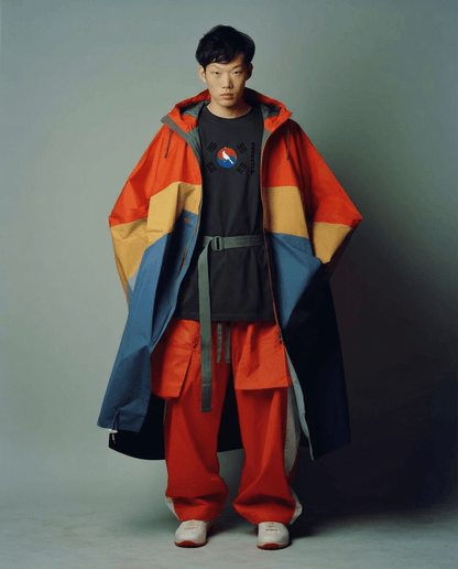 Person wearing a colorful coat and red pants against a plain background