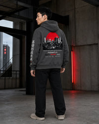 A man wearing a dark gray hoodie with a large red and black city graphic on the back, standing in a concrete industrial interior.