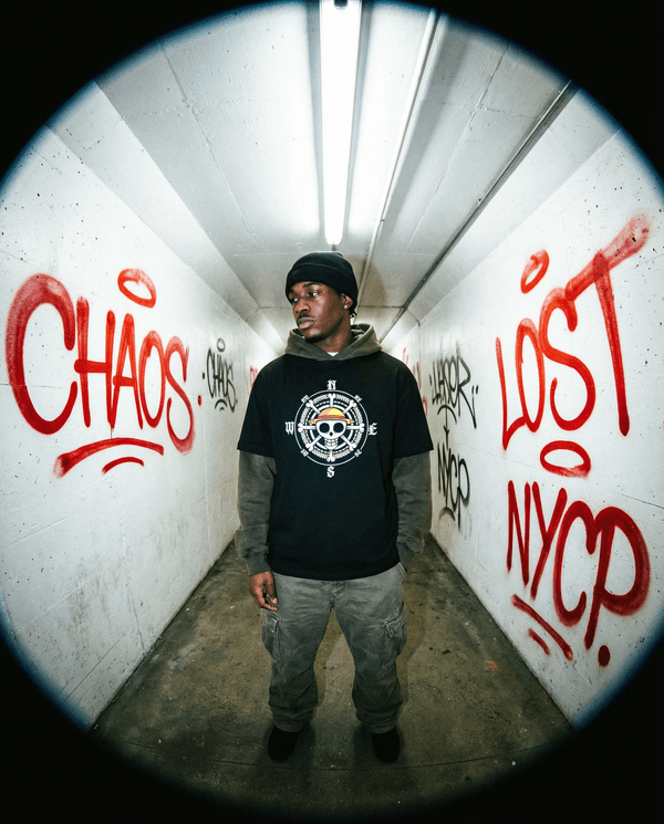 Model wearing One Piece Essential Cotton T-Shirt in black with compass and skull design, styled for urban streetwear in graffiti tunnel.