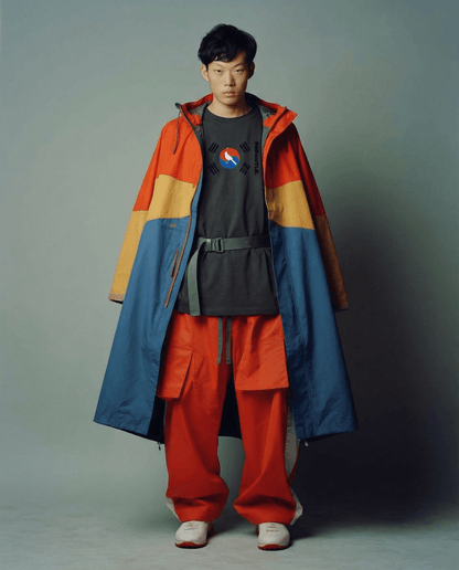 Person wearing a colorful jacket and red pants against a plain background