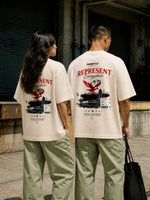 Two models standing side-by-side from behind wearing matching cream-colored t-shirts with a large red and black graphic print on the back, paired with light green cargo pants in an urban alleyway.