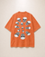 An orange short-sleeve t-shirt with a graphic print of multiple white and black skulls arranged in a circular pattern on the back, displayed against a light beige background.