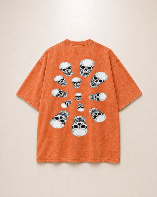 An orange short-sleeve t-shirt with a graphic print of multiple white and black skulls arranged in a circular pattern on the back, displayed against a light beige background.