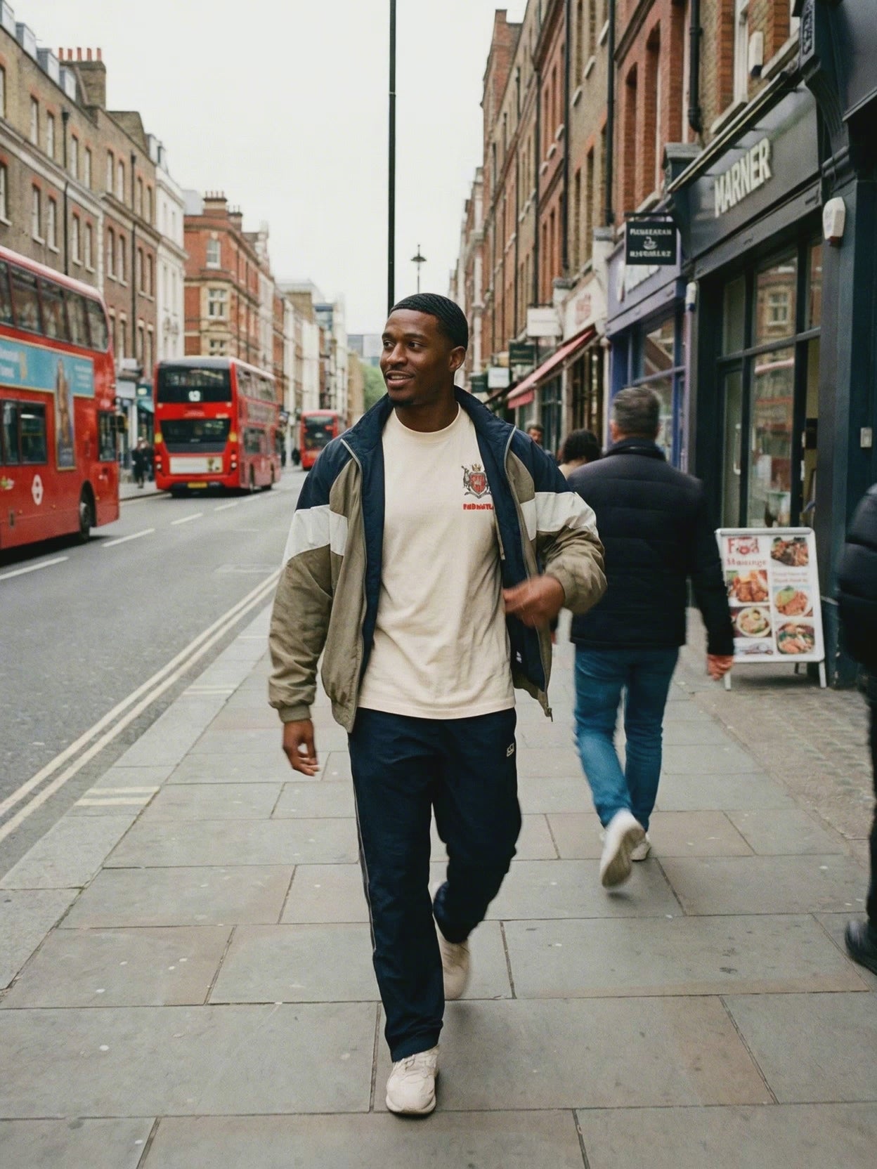Man wearing Armor of God Essential Cotton T-Shirt in beige, styled with a sporty jacket and navy track pants on a city street. Soft, breathable, durable cotton tee for daily casual wear.